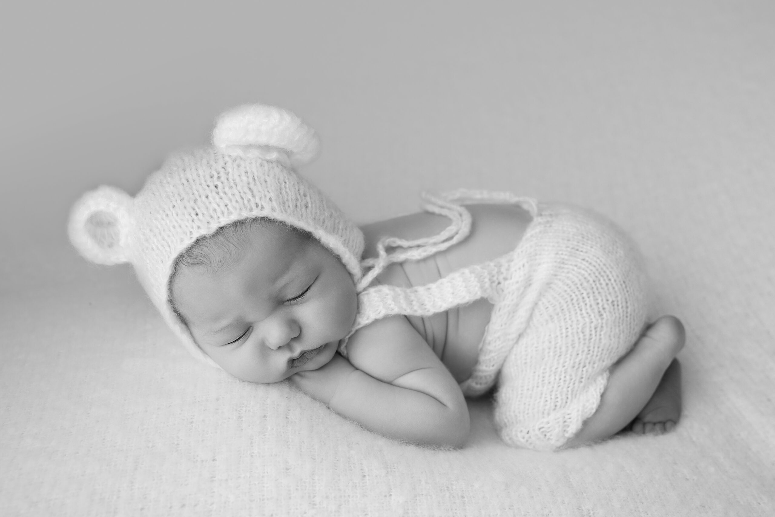 baby curled up on a bed, wearing a white knit hat