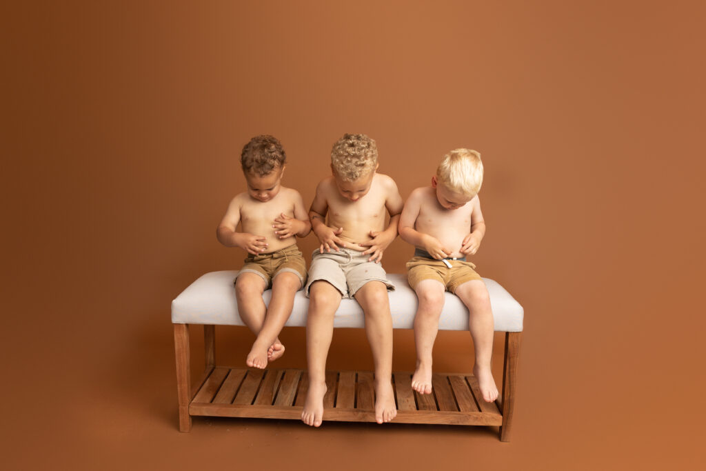 Three boys with different skin tones laughing together while playfully looking at their bellies during a family photography session in Northeast Ohio.
