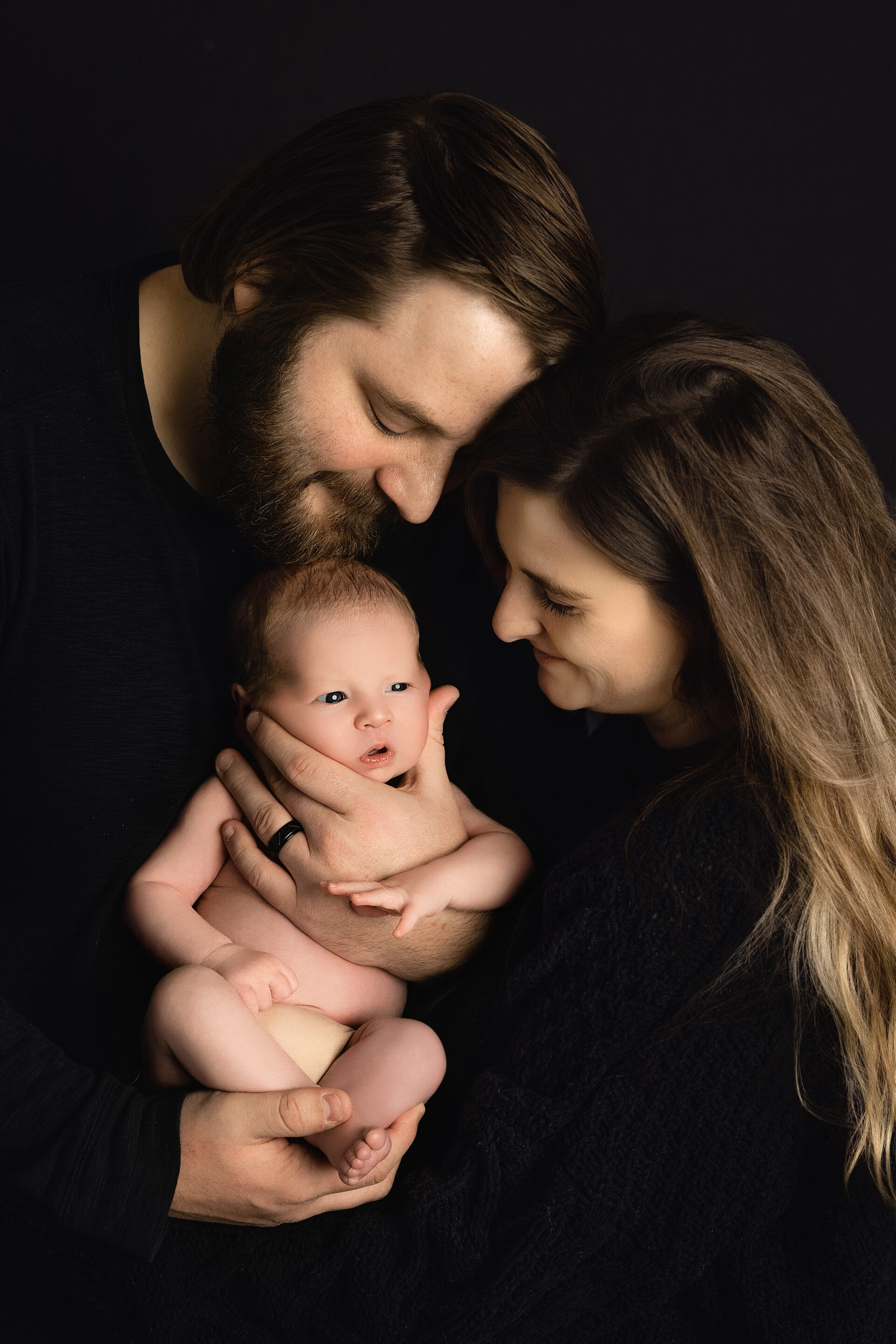family of 3 joyfully holding their newborn baby boy