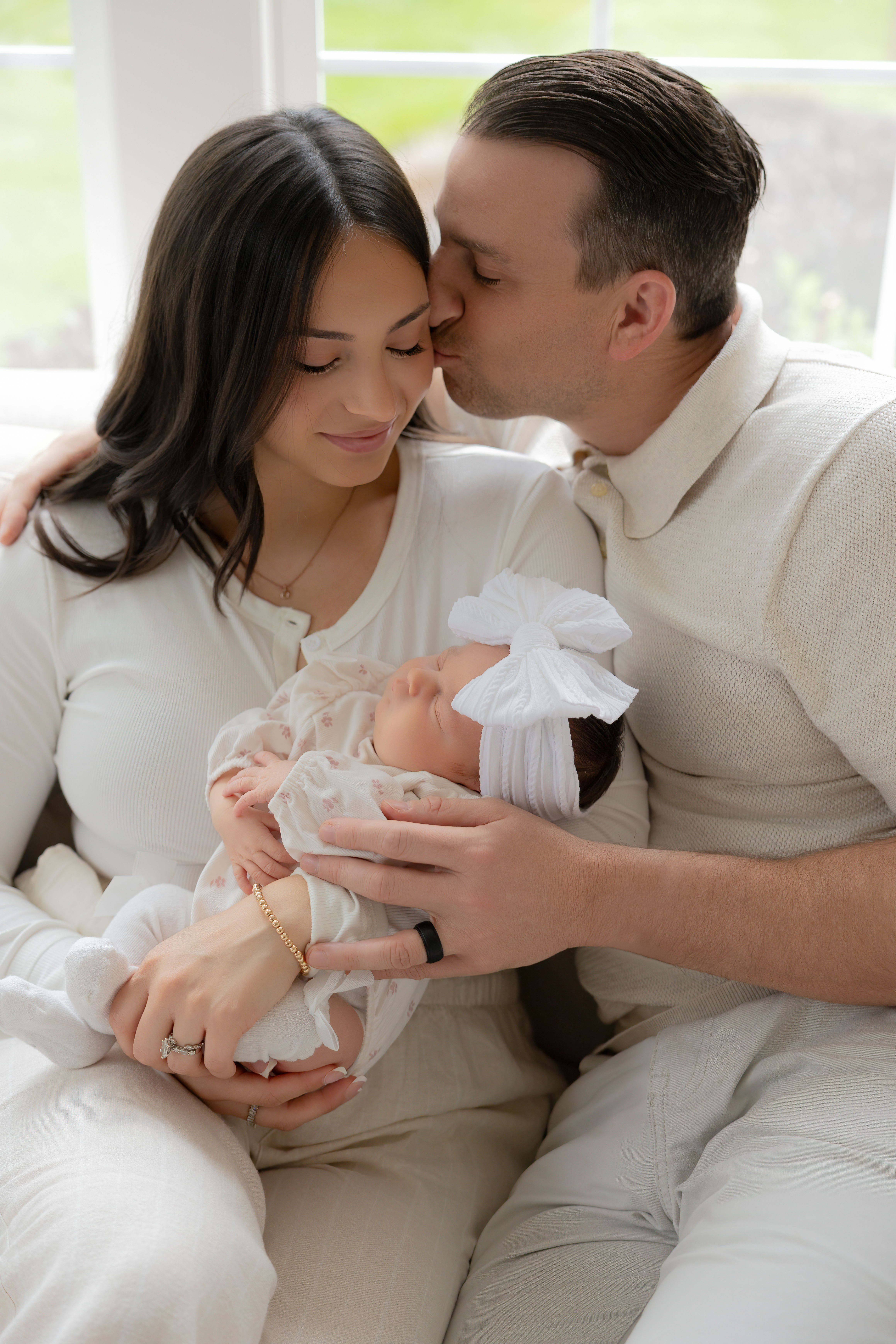 New father kissing his wife as she holds their baby girl; newborn photography in Medina county ohio