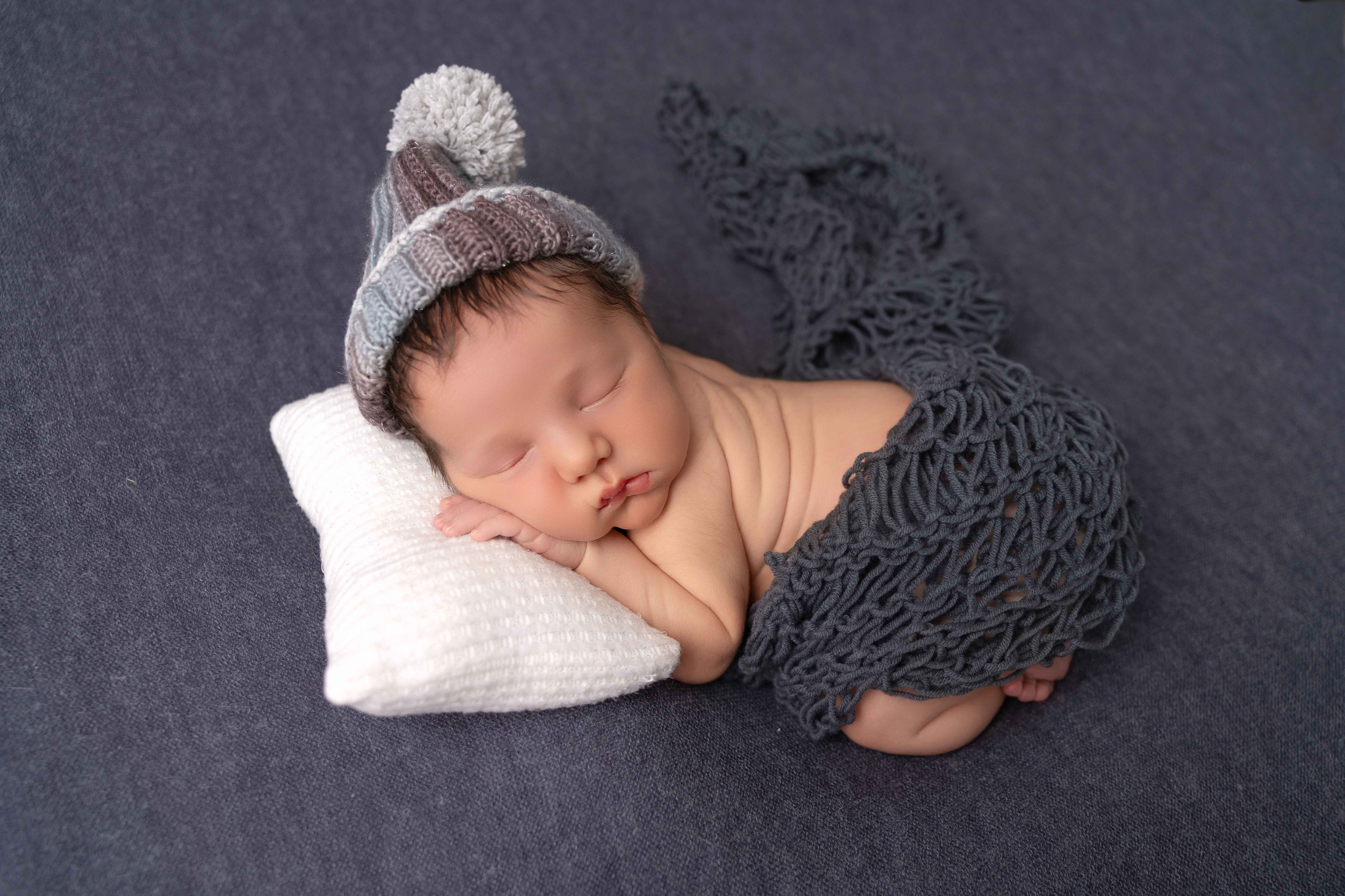 sleeping baby boy, curled up on a white pillow wearing a blue cap; newborn and family photography in medina county ohio