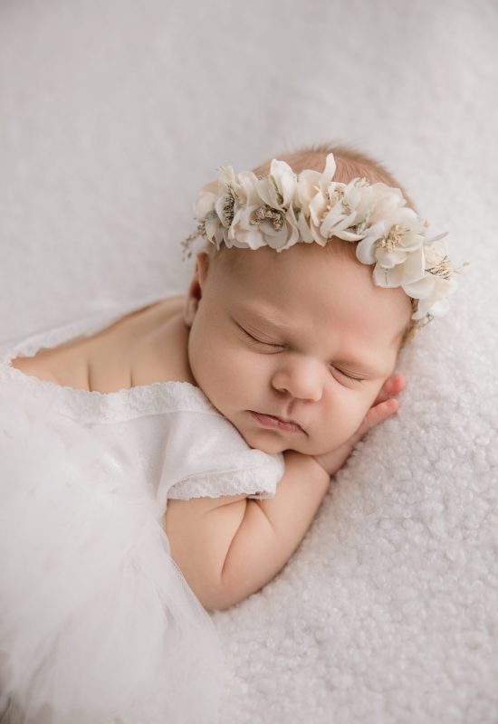 baby girl in white flower headband and sleeping on a soft white blanket