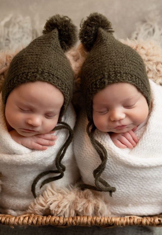 sweet photo of twins in a basket with matching hats, bundled in soft white blankets
