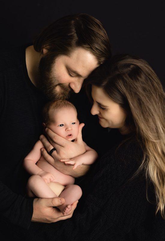 family of 3 joyfully holding their newborn baby boy