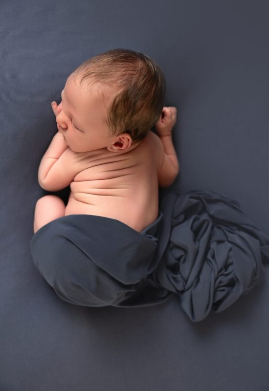 baby boy all curled up sleeping on blue blanket, showing off his chubby back rolls